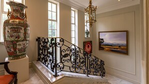 A grand staircase with ornate black railings, a large decorative vase, and a landscape painting on the wall.