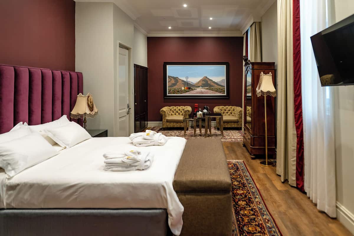 Ein Hotelzimmer mit einem großen Bett, einem Schreibtisch mit zwei Stühlen, einem Fernseher und einem Gemälde an der Wand.