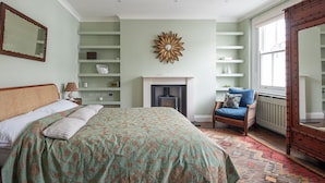 Een slaapkamer met een bed, een stoel, een open haard, planken en een grote spiegel.