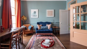 Een gezellige woonkamer met een blauwe bank, een houten eettafel en een kamerkleed met een patroon.