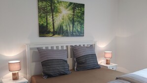 A neatly made bed with a brown mattress and two pillows, flanked by white nightstands with lamps, in a room with a white ceiling and walls.