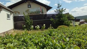 A building with a sign reading "Kellerhof 18" and a garden with green shrubs in the foreground.