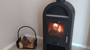 A wood-burning stove with a glass door, a fire burning inside, and a basket of firewood beside it.