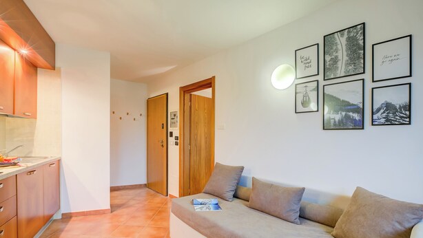 Een moderne woonkamer met een bank, een keuken met kasten, en een gang met houten deuren.