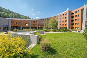 Een modern gebouw met meerdere verdiepingen, een binnentuin met gras en beplanting, en een berg op de achtergrond.