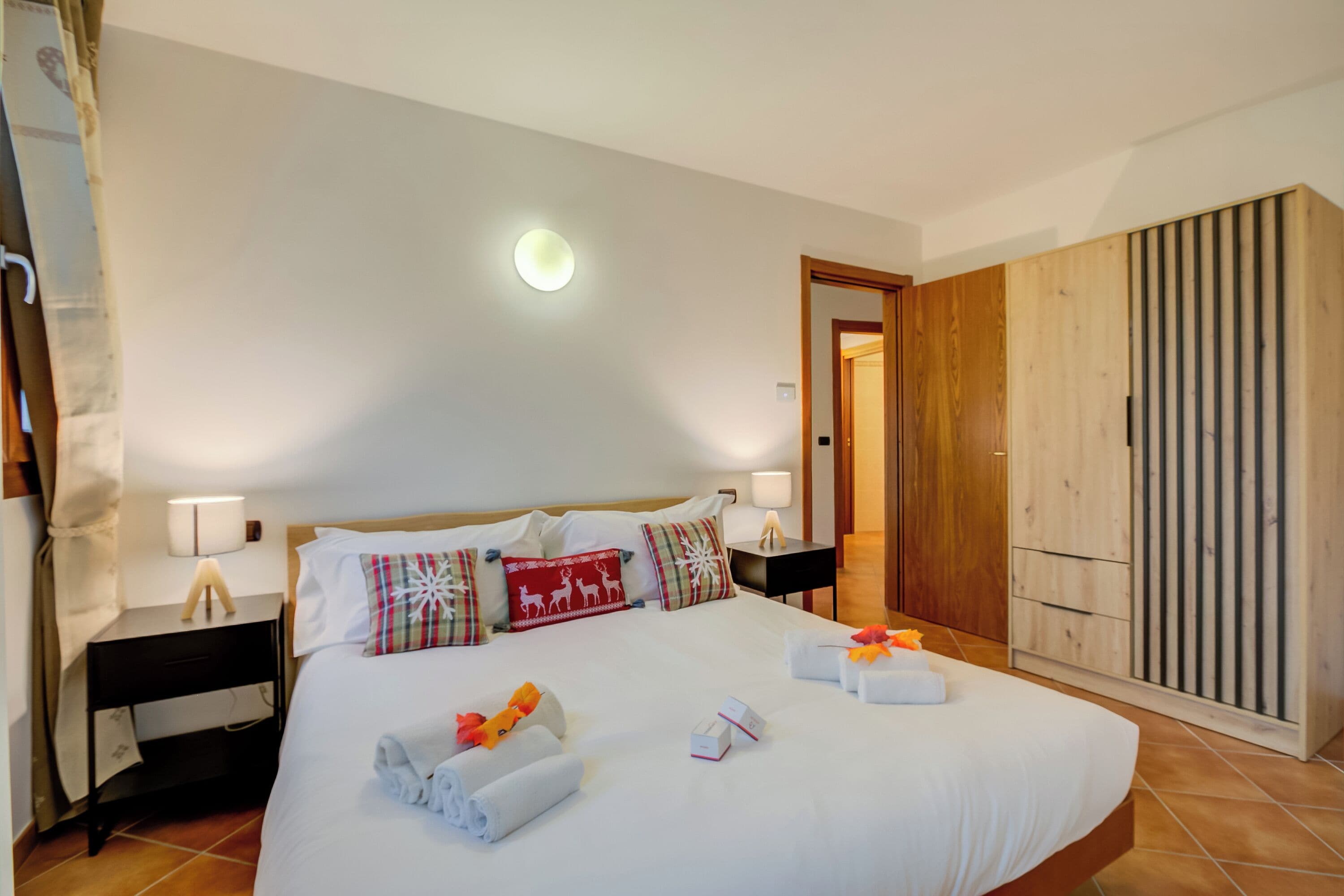 A hotel room with a large bed, a wooden wardrobe, and a nightstand with a lamp.