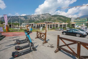 Uma área de estacionamento com scooters elétricas, uma cerca de madeira e montanhas ao fundo.