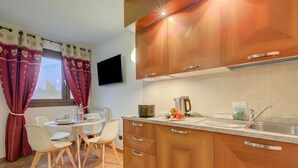 A modern kitchen with wooden cabinets, a stainless steel sink, and a dining area with white chairs and a table.