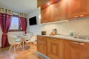 Cozinha moderna com armários de madeira, pia de aço inoxidável e área de jantar com cadeiras brancas e uma mesa.
