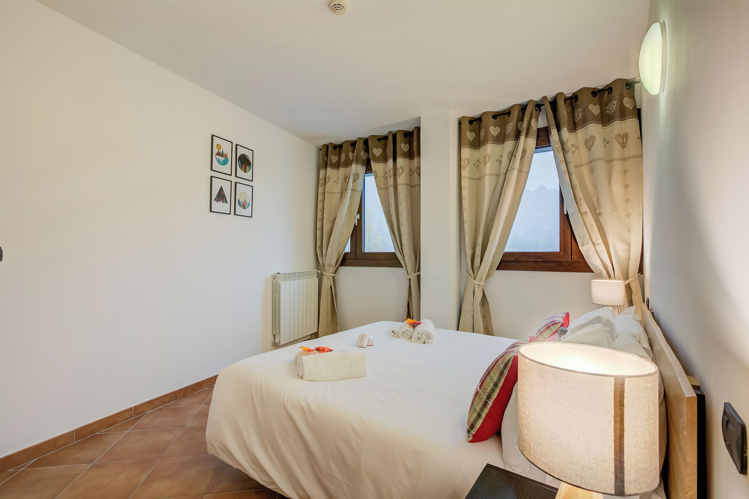 Une chambre d’hôtel avec un lit, une lampe de chevet, une fenêtre avec des rideaux et un radiateur.
