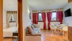 A room with a sofa, a dining table with chairs, a TV, and a bed.