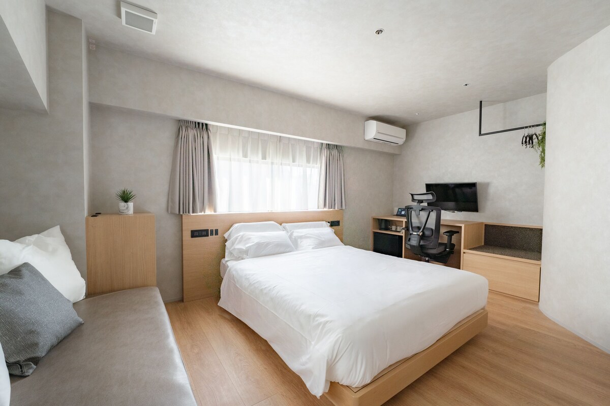A modern hotel room with a large bed, a desk with a chair, and a television.