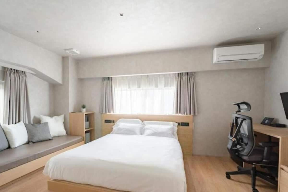 A modern hotel room with a large bed, a desk with a chair, and an air conditioning unit.