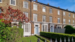A row of brick townhouses with white-framed windows, a blue door, and a well-maintained hedge in the front yard. - New Holgate (York)