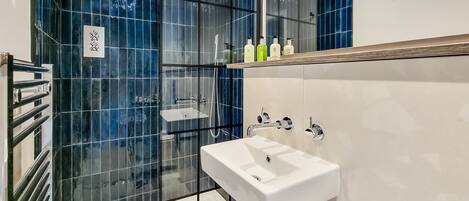 Un baño moderno con cabina de ducha de vidrio, un lavabo blanco y un estante con artículos de aseo.