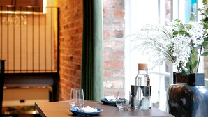 A dining area with a brick wall, wooden table, chairs, and a large window. - New Holgate (York)