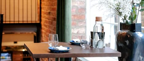 A dining area with a brick wall, wooden table, chairs, and a large window.