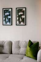 A neutral-toned sofa with a green pillow and two abstract paintings on the wall.
