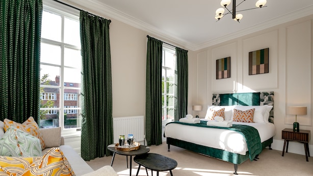 A hotel room with a large bed, a sofa, a small table, and a view of buildings outside. - New Holgate (York)