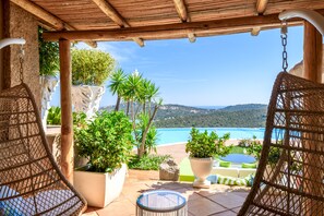 A covered outdoor seating area with wicker chairs, potted plants, and a view of the sea. - Villa Felix, Pantogia  (Pantogia)