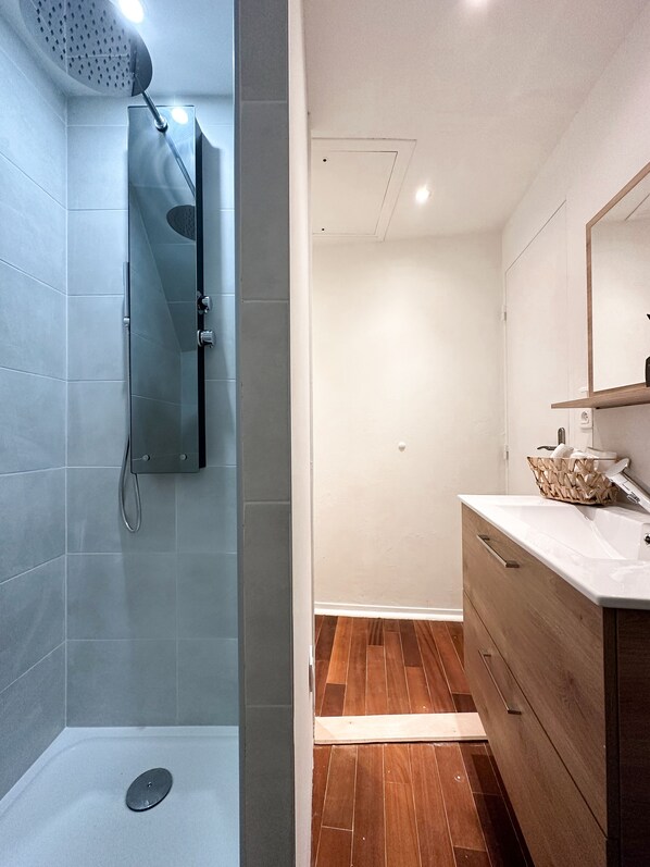 A modern bathroom with a shower, a wooden vanity, and a large mirror.