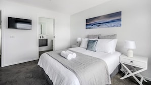 Une chambre moderne avec un grand lit, un téléviseur à écran plat, un tableau représentant un paysage marin et un dressing.