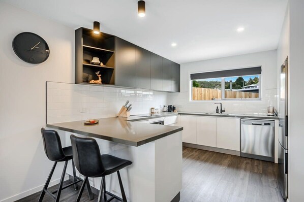 A modern kitchen with a central island, black bar stools, a built-in oven, and a window with a view of the outdoors.