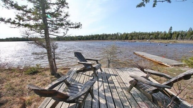A wooden deck with Adirondack chairs overlooking a lake, surrounded by trees. - Red Barn | Waterfront | Private | Tobermory | A-Frame | Pet Friendly (Tobermory)