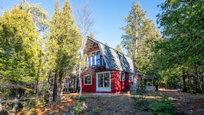 A red cabin with a blue balcony, surrounded by dense forest. - Red Barn | Waterfront | Private | Tobermory | A-Frame | Pet Friendly (Tobermory)
