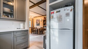 A modern kitchen with grey cabinets, a white refrigerator, and a dining area with wooden chairs and a table. - Red Barn | Waterfront | Private | Tobermory | A-Frame | Pet Friendly (Tobermory)