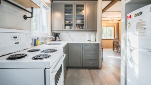 A modern kitchen with grey cabinets, a white stove, and a refrigerator. - Red Barn | Waterfront | Private | Tobermory | A-Frame | Pet Friendly (Tobermory)