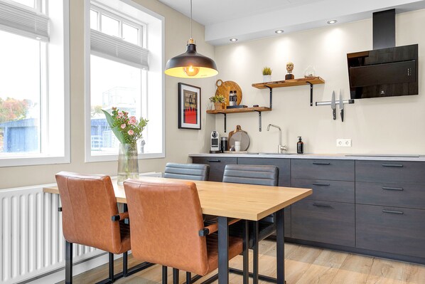Cozinha moderna com mesa de jantar de madeira, cadeiras de couro e luminária pendente.