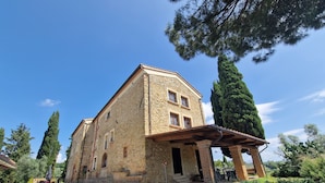 Un edificio de piedra con un porche cubierto, rodeado de árboles y grava.
