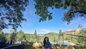 Una persona sentada en un banco en un jardín con piscina y un edificio al fondo.
