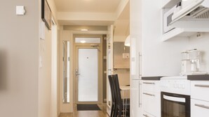 A narrow kitchen with a stove, microwave, and cabinets. A dining table and chairs are visible in the background. - Klostergaarden leilighetshotell (Stavanger)