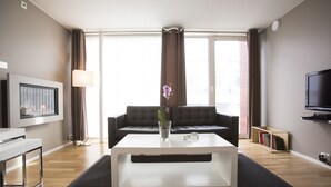A modern living room with a white coffee table, a black sofa, a TV, and a bookshelf. - Klostergaarden leilighetshotell (Stavanger)