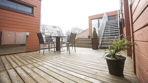 A wooden deck with outdoor furniture, a potted plant, and a staircase leading to an upper level. - Klostergaarden leilighetshotell (Stavanger)
