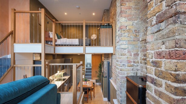 Ein Loft-Zimmer mit einem erhöhten Zwischengeschoss, einer Holztreppe und einer Ziegelwand.