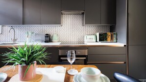 A modern kitchen with a herringbone tile backsplash, stainless steel appliances, and a wooden dining table with a potted plant. - Exposed Brick Flat Finsbury Park (London)