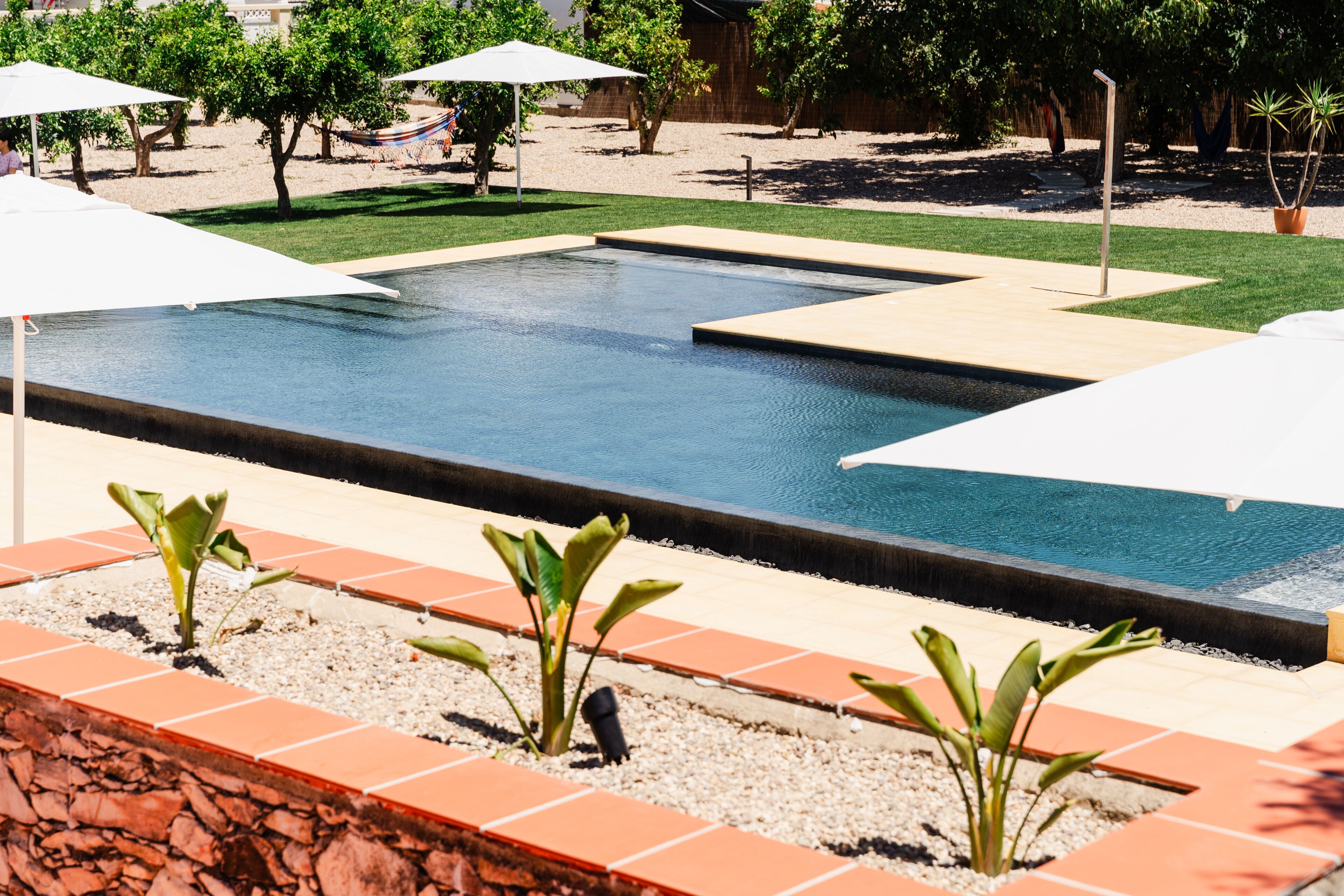 A swimming pool with a tiled deck, surrounded by potted plants and umbrellas.
