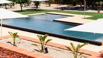 A swimming pool with a tiled deck, surrounded by potted plants and umbrellas.