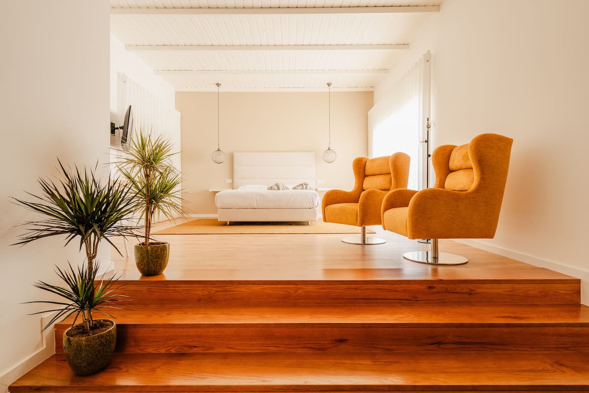 A modern living room with a wooden staircase, a white sofa, and two orange armchairs.