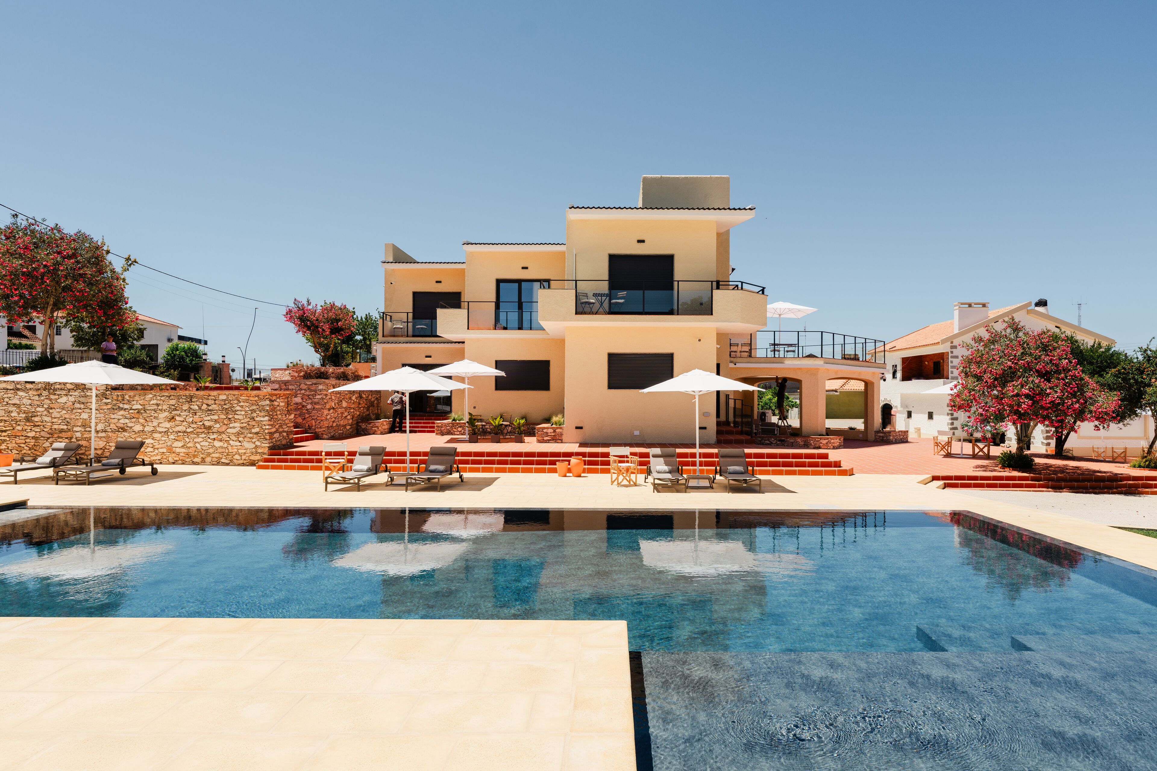 A modern multi-story building with a swimming pool, outdoor seating, and a stone wall.