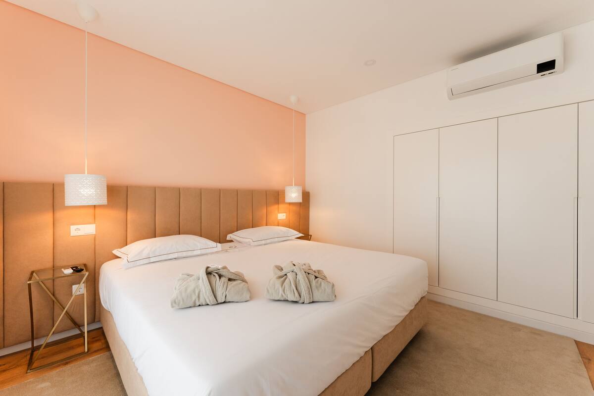 A hotel room with a large bed, bedside tables, a wardrobe, and an air conditioning unit.