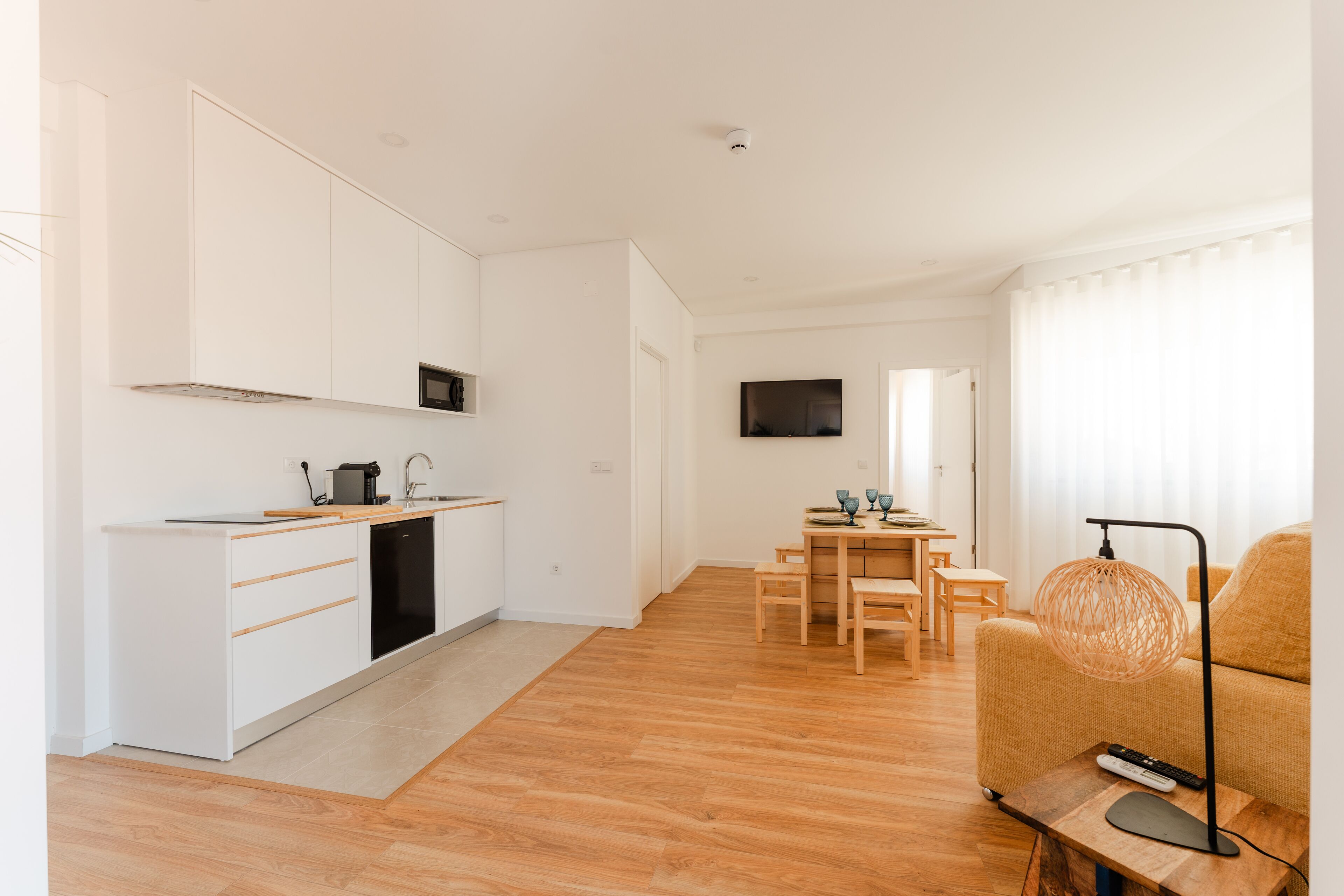 A modern kitchen with white cabinets, a black dishwasher, and a wooden dining table with chairs.