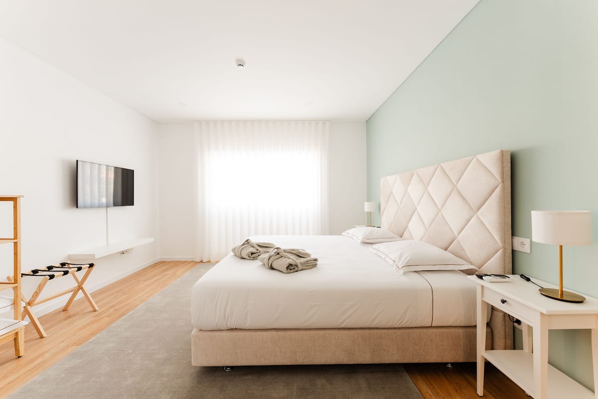 A modern bedroom with a large bed, a flat-screen TV, a bedside table with a lamp, and a wooden floor.