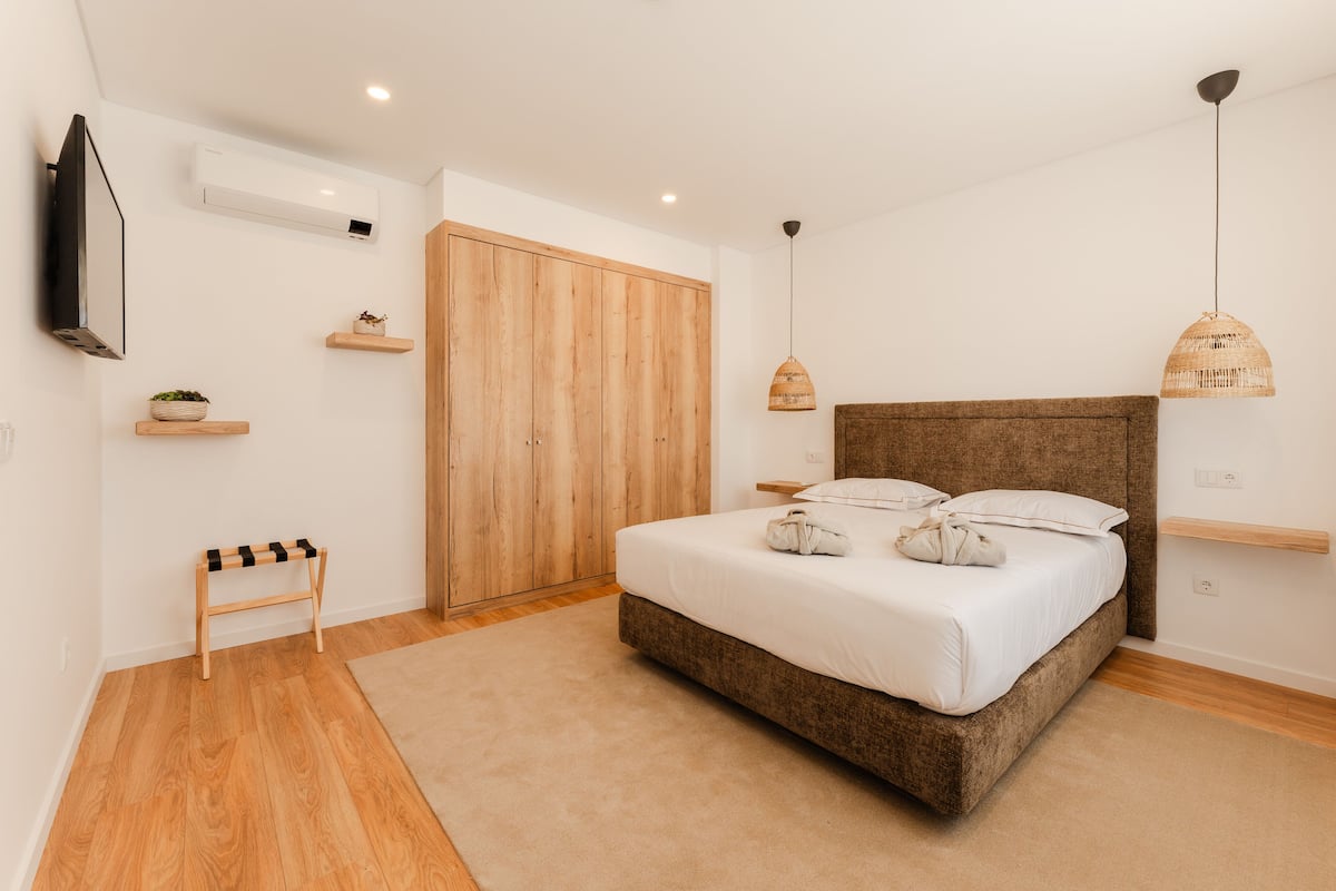 A bedroom with a bed, wooden wardrobe, and a TV mounted on the wall.