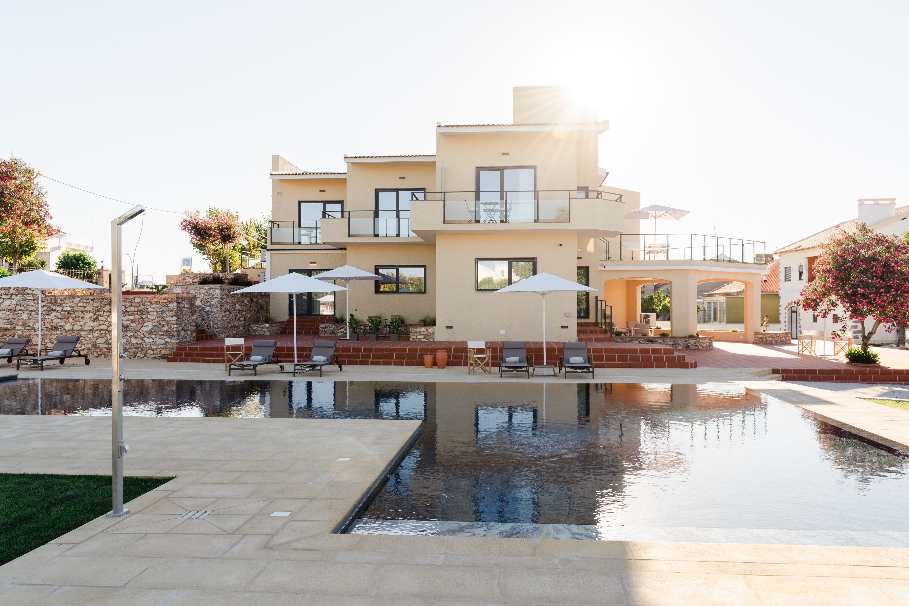 Un bâtiment moderne à deux étages, doté d’une piscine, d’un espace extérieur aménagé et d’un mur en pierre.