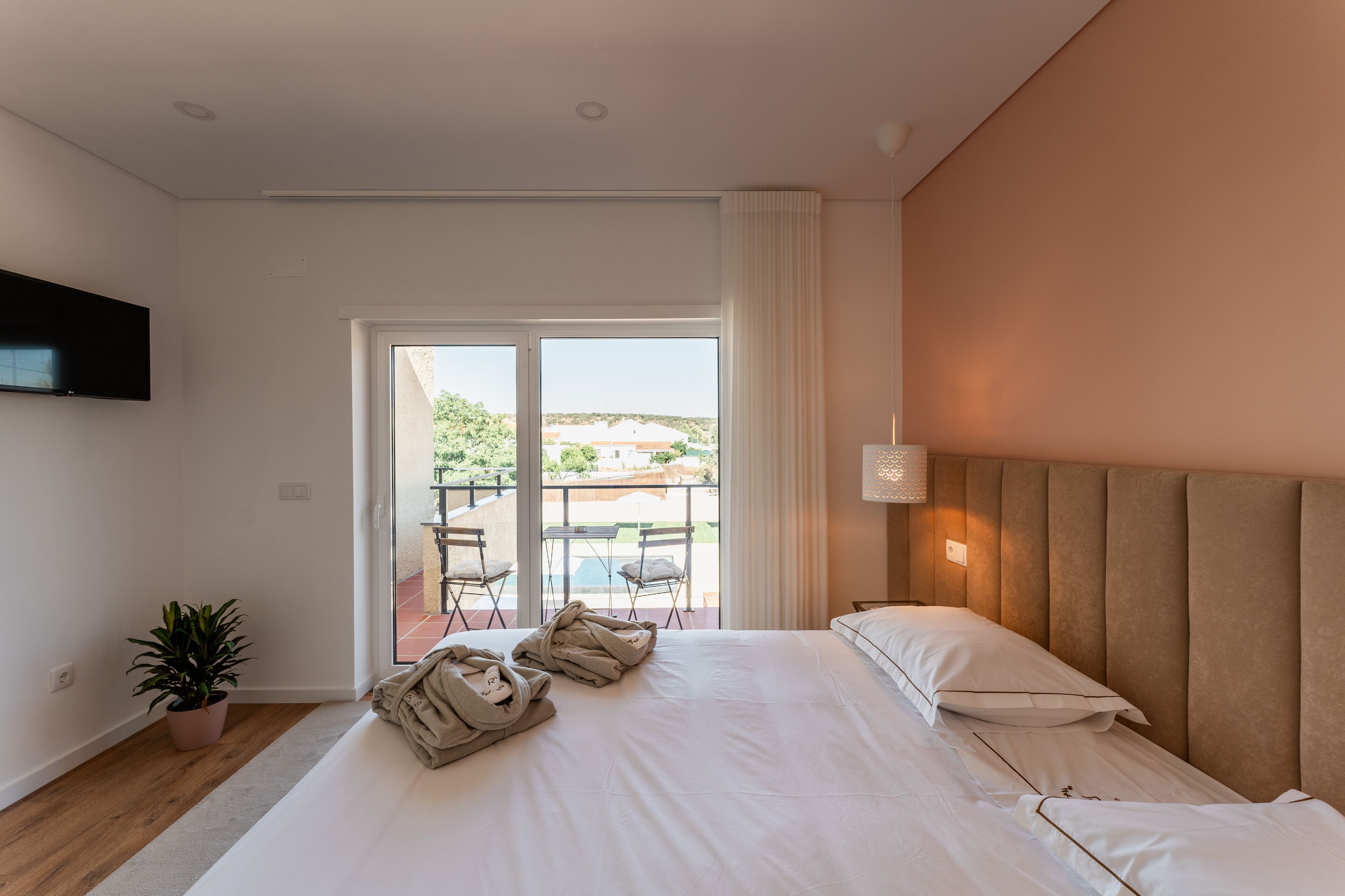 Habitación de hotel con una cama grande, una planta en maceta, un televisor de pantalla plana y un balcón con mobiliario exterior.