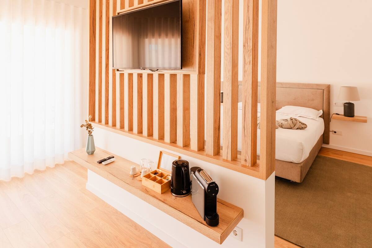 A modern hotel room with a wooden slat wall, a mounted TV, a bedside table with a lamp, and a bed.